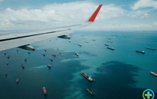 dozens of cargo ships stranded in a bay, photo taken from plane window with wing visible